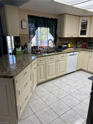 Kitchen featuring a toaster, dishwasher, a sink, stone counters, and cream cabinets