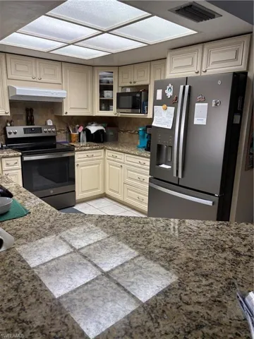 Kitchen with fridge, visible vents, stove, exhaust hood, and light stone counters