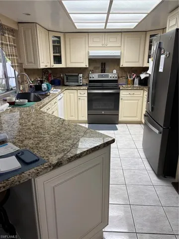 Kitchen with stove, cream cabinetry, exhaust hood, dark stone counters, and fridge