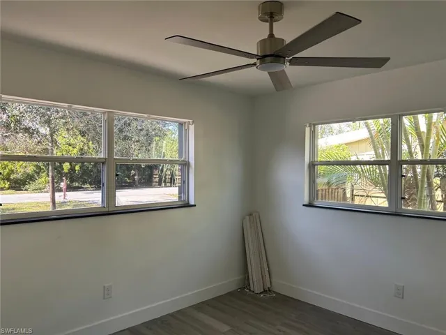 Empty room with dark wood-style flooring, healthy amount of natural light, and a ceiling fan