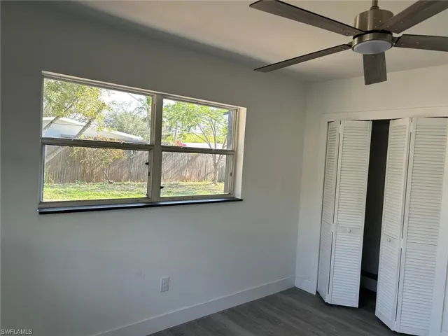 Unfurnished bedroom with a closet, multiple windows, a ceiling fan, and dark wood-style flooring