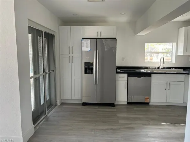 Kitchen featuring appliances with stainless steel finishes, white cabinets, a textured wall, and dark countertops