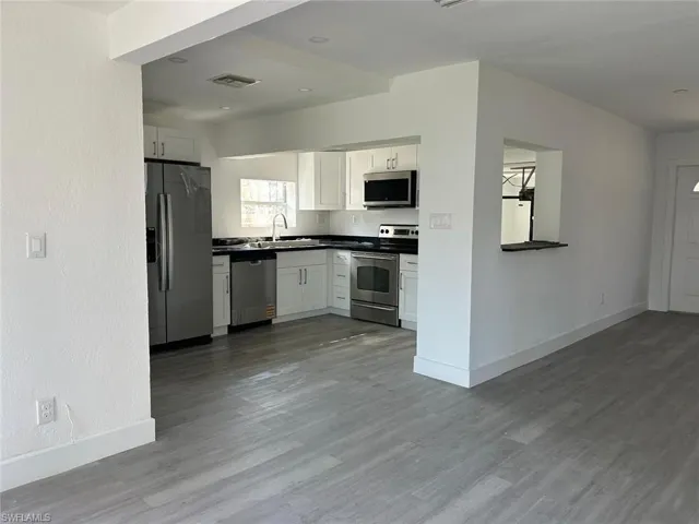 Kitchen with appliances with stainless steel finishes, white cabinetry, dark countertops, and dark wood-style flooring