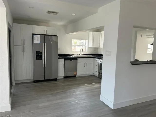 Kitchen featuring appliances with stainless steel finishes, dark countertops, white cabinets, light wood-type flooring, and recessed lighting