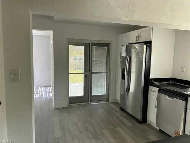 Kitchen featuring a textured wall, stainless steel appliances, white cabinetry, and dark wood-style flooring