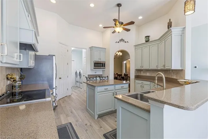 Kitchen featuring decorative backsplash, arched walkways, gray cabinetry, recessed lighting, and a high ceiling