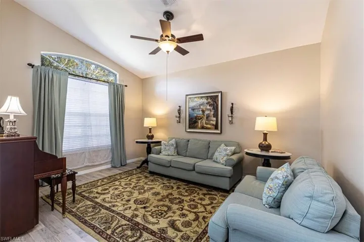 Living room with lofted ceiling, light wood-style floors, and ceiling fan