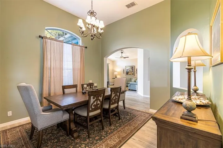 Dining space featuring arched walkways, light wood-type flooring, a ceiling fan, a chandelier, and high vaulted ceiling