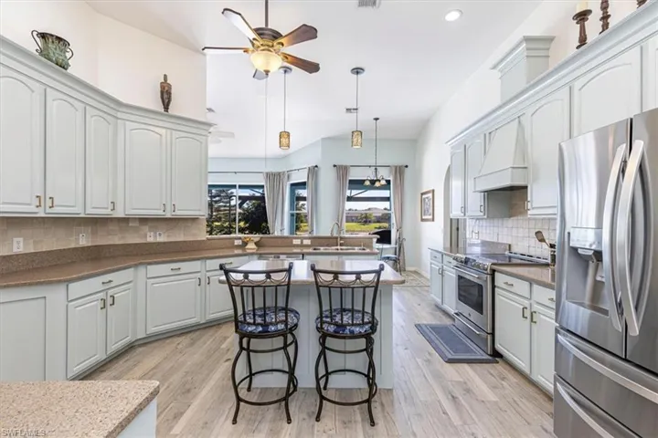 Kitchen with decorative backsplash, appliances with stainless steel finishes, a breakfast bar area, hanging light fixtures, and premium range hood
