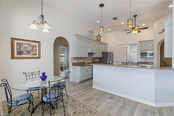 Kitchen featuring arched walkways, decorative light fixtures, light stone countertops, stainless steel appliances, and a towering ceiling