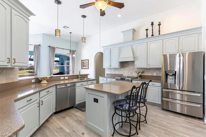 Kitchen with appliances with stainless steel finishes, a breakfast bar area, light stone countertops, premium range hood, and decorative light fixtures