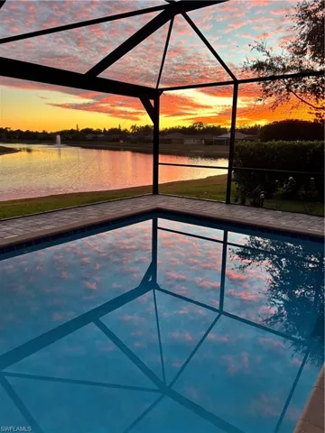 Pool at dusk featuring an outdoor pool, glass enclosure, a sunroom, and a water view