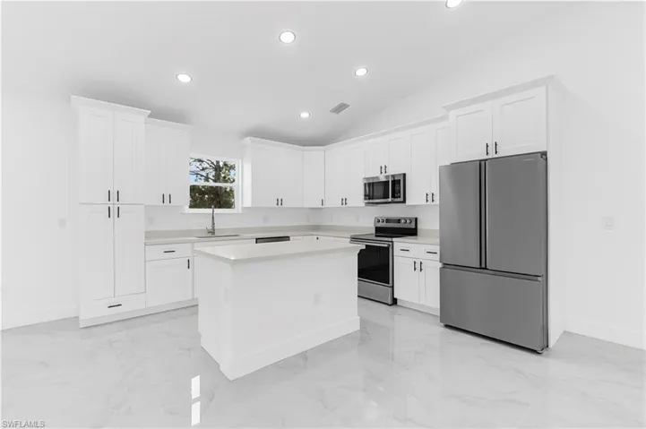 Kitchen with appliances with stainless steel finishes, white cabinetry, recessed lighting, a kitchen island, and light marble finish floors