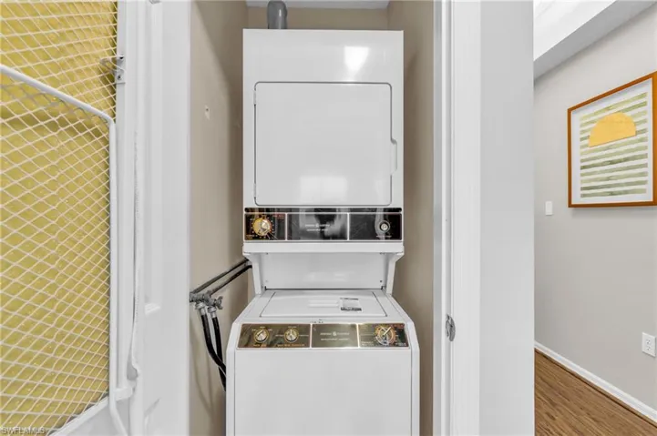 Clothes washing area with stacked washer and clothes dryer and hardwood / wood-style flooring
