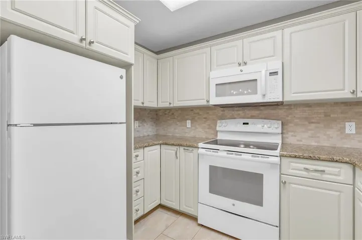 Kitchen featuring decorative backsplash, white cabinetry, light tile patterned floors, and white appliances