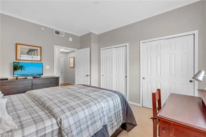 Bedroom with light carpet, ornamental molding, and multiple closets