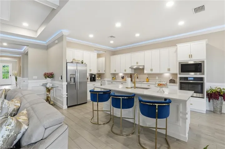 Kitchen with white cabinets, open floor plan, wainscoting, appliances with stainless steel finishes, and crown molding