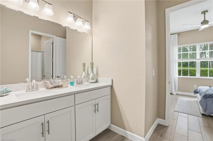 Full bathroom featuring double vanity, curtained shower, ensuite bath, wood finish floors, and a ceiling fan