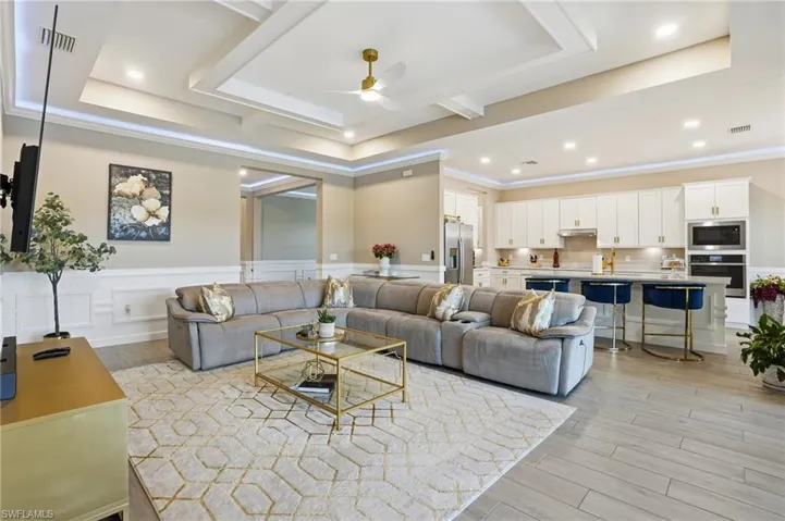 Living area featuring light wood-style flooring, ceiling fan, a raised ceiling, crown molding, and recessed lighting