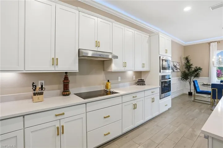 Kitchen featuring white cabinetry, under cabinet range hood, appliances with stainless steel finishes, crown molding, and light wood-style flooring