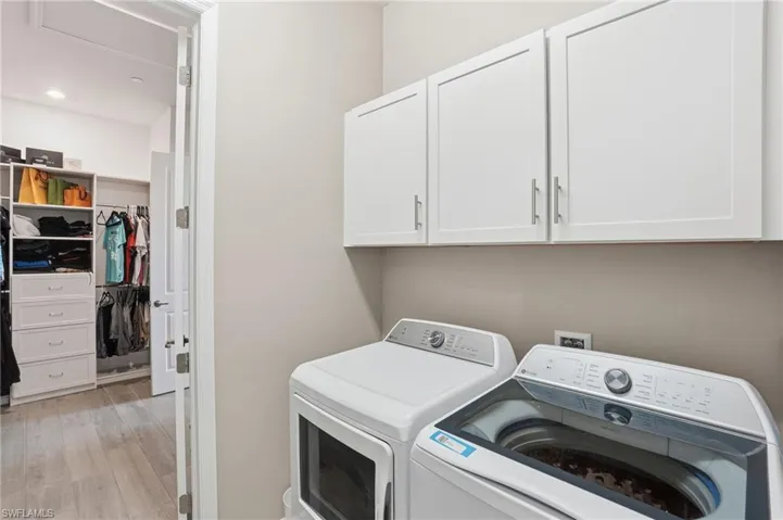 Washroom featuring washer and clothes dryer, cabinet space, light wood-type flooring, and recessed lighting