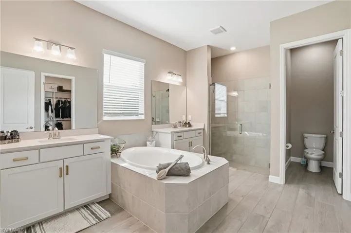 Bathroom featuring two vanities, a shower stall, a spacious closet, wood finish floors, and a garden tub