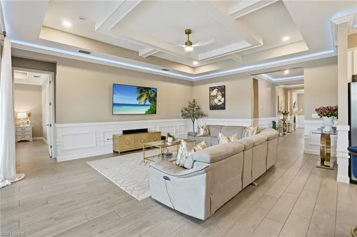 Living room with light wood-type flooring, a ceiling fan, a decorative wall, wainscoting, and a tray ceiling