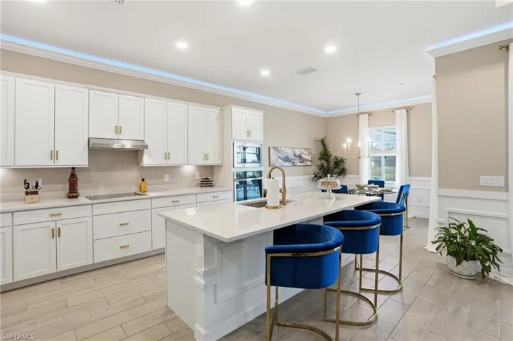 Kitchen featuring pendant lighting, white cabinets, a kitchen island with sink, wood tiled floors, and a kitchen bar