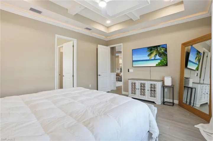 Bedroom with ornamental molding, light wood-type flooring, coffered ceiling, and a tray ceiling