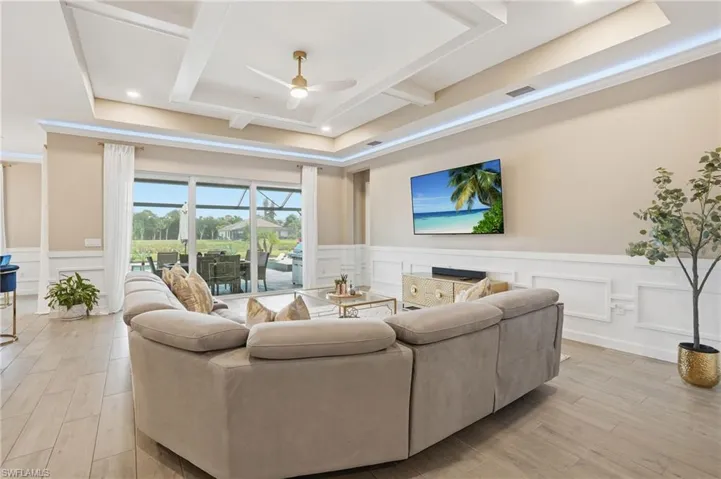 Living area featuring a ceiling fan, a tray ceiling, a decorative wall, light wood finished floors, and a wainscoted wall