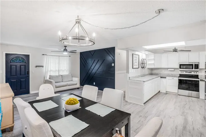 Dining space featuring ceiling fan with notable chandelier, light wood-type flooring, and a textured ceiling