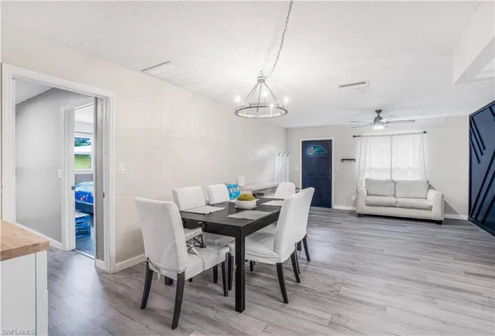 Dining area with baseboards, a textured ceiling, ceiling fan with notable chandelier, and light wood finished floors