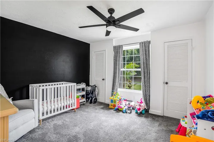 Carpeted bedroom featuring a ceiling fan, a crib, and a textured ceiling