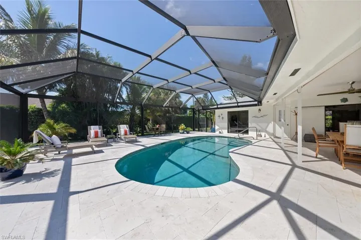 View of pool with glass enclosure, ceiling fan, and a patio area