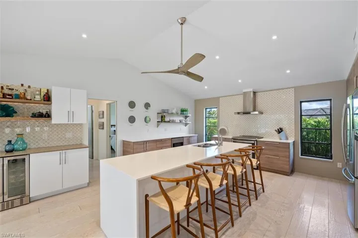 Kitchen featuring beverage cooler, white cabinetry, a center island with sink, and wall chimney range hood
