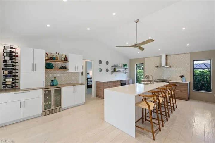 Kitchen with wall chimney exhaust hood, white cabinets, beverage cooler, and a spacious island
