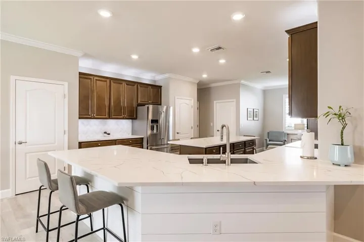 Kitchen with a breakfast bar, high end fridge, sink, tasteful backsplash, and ornamental molding