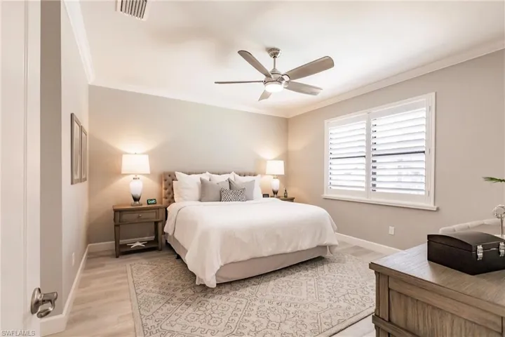 Bedroom with ceiling fan, ornamental molding, and light wood-type flooring
