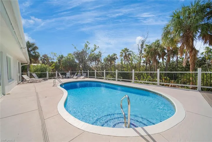 In-ground swimming pool with a curved design, concrete pool deck, and white perimeter fencing, set against a backdrop of mature palm trees