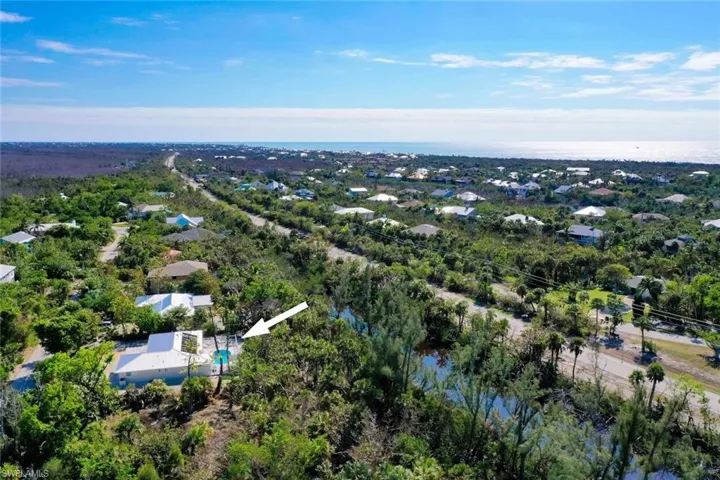 Aerial perspective of residential property featuring a private swimming pool, light-colored roof, and proximity to coastal water