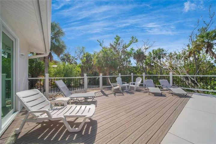 Expansive wood-finish deck featuring white railing with black metal balusters and mature perimeter trees