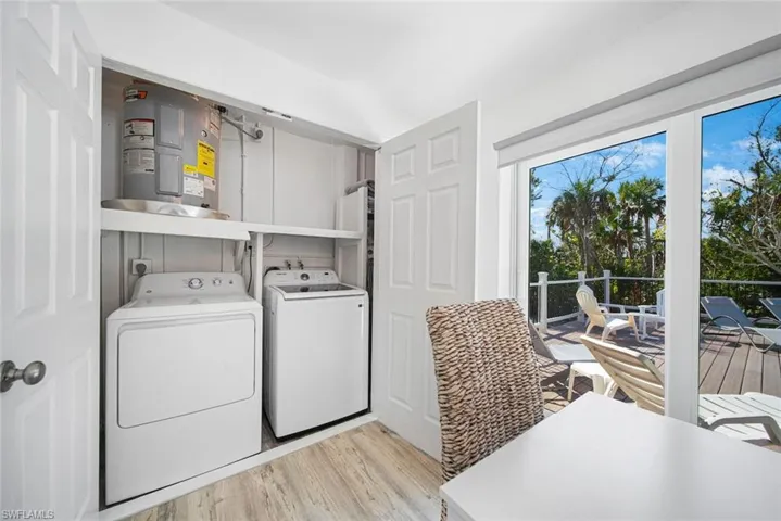 Laundry closet featuring built-in shelving, water heater, and side-by-side laundry appliances, accented by wood-finish flooring and full-height sliding glass doors opening to an exterior deck