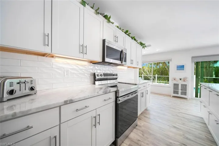 Kitchen featuring white shaker-style cabinetry, stone-patterned countertops, a glossy subway tile backsplash, stainless steel appliances, and wood-finish flooring