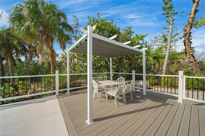 Elevated composite deck featuring a pergola, white railing with vertical black balusters, and surrounding mature tropical vegetation