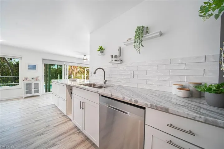 Kitchen featuring stone-patterned countertops, white shaker-style cabinetry, stainless steel dishwasher, subway tile backsplash, and wood-finish flooring