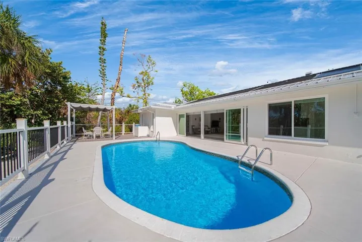 In-ground pool surrounded by a concrete patio, retractable glass wall system, white stucco exterior, and metal roofing