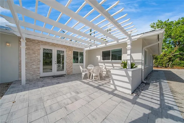 Back patio featuring a white pergola, light-toned stone veneer accent wall, paved stone surface, and built-in masonry planter