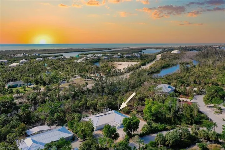 Aerial perspective of a property featuring a light-toned hipped roof, mature surrounding vegetation, and proximity to coastal waterways