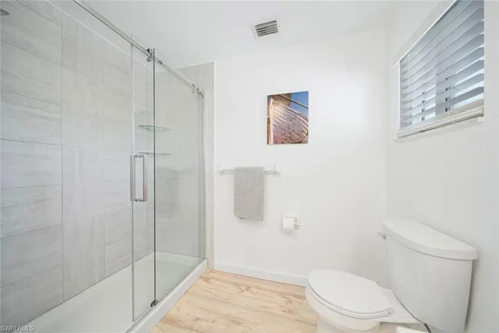 Walk-in shower with floor-to-ceiling tile surround and sliding glass doors, wood-finish flooring, and horizontal window blinds