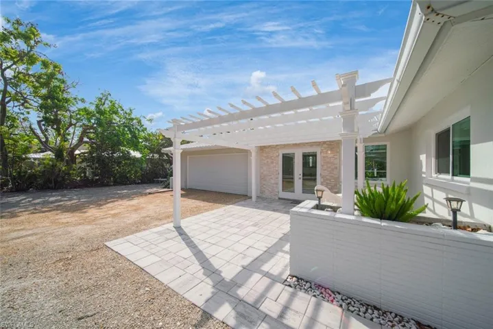 Outdoor living space featuring a white pergola, paver patio, stone-accented exterior wall, and low-profile painted brick planter